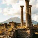 A photo of ancient columns at the ruins in Pompeii with Mount Vesuvius in the background.