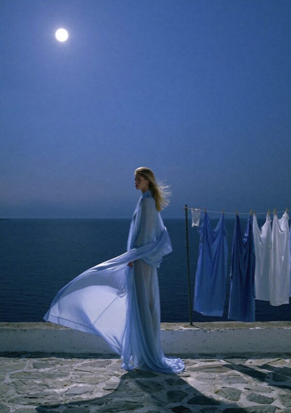 Victoria Van Der Berg on a Capri rooftop at night under a full moon, wearing a flowing pale blue dress billowing in the wind, blue and white laundry on the line, sea in the distance