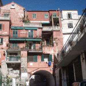 An Amalfi street with a terracotta pink building green shutters and a miniature presepe village display built into the stone wall beside the archway