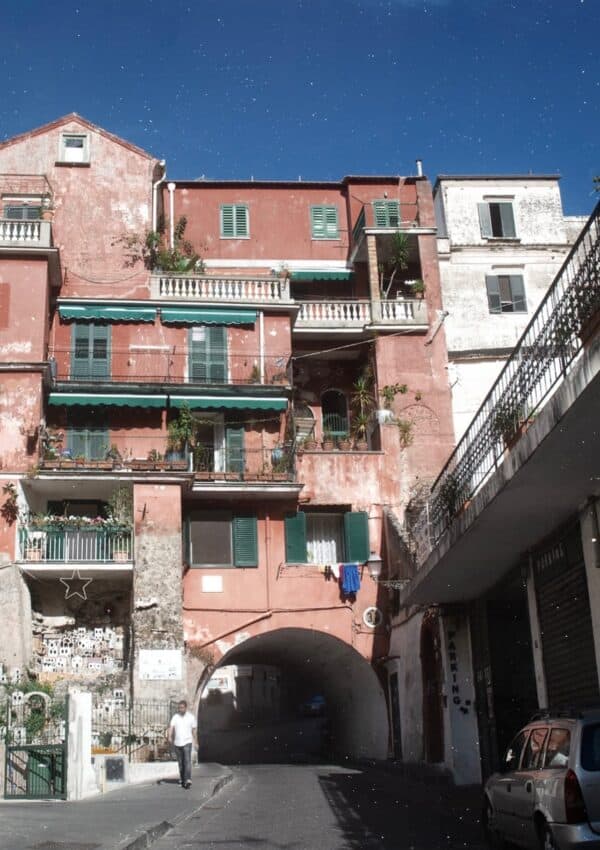 An Amalfi street with a terracotta pink building green shutters and a miniature presepe village display built into the stone wall beside the archway