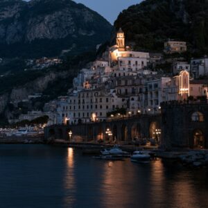 An Amalfi Coast town at dusk with lights coming on, framed by a lemon tree