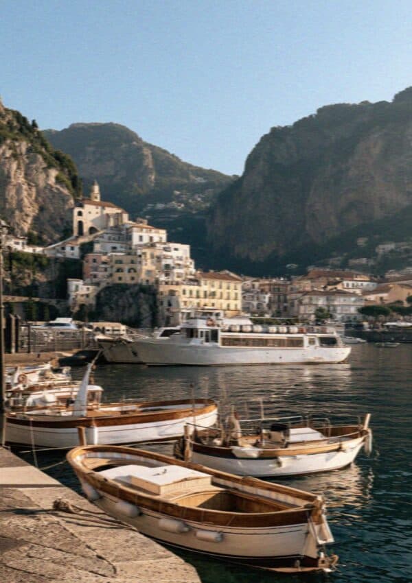 Wooden boats and a yacht below an Amalfi Coast town with cliffs