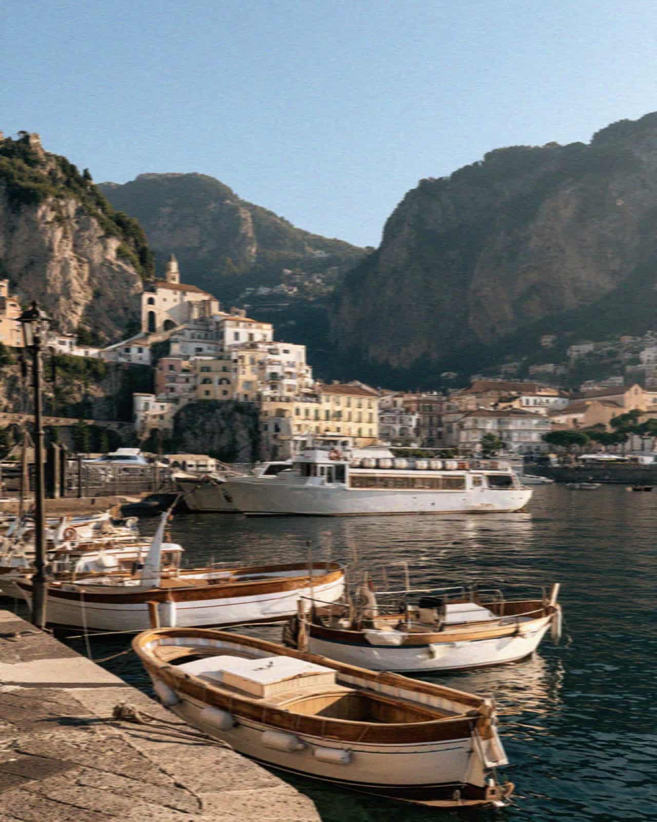 Wooden boats and a yacht below an Amalfi Coast town with cliffs