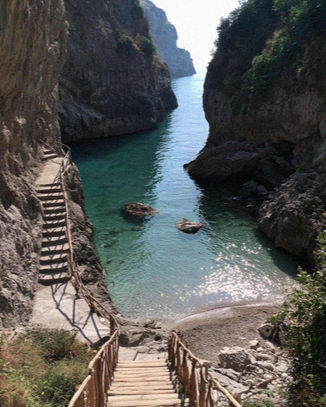 The hidden cove of Duoglio near Amalfi with turquoise water, cliffs and a wooden stair down to the beach