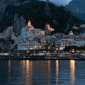 The Amalfi coast town at night seen from the water with lights reflecting