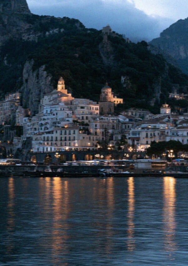 The Amalfi coast town at night seen from the water with lights reflecting