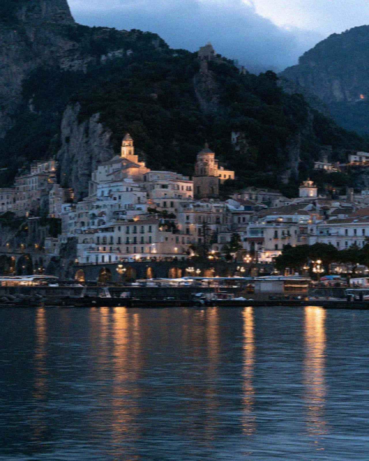 The Amalfi coast town at night seen from the water with lights reflecting