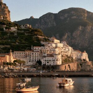 The town of Amalfi seen from the sea at golden hour, houses stacked on the cliff above the harbour