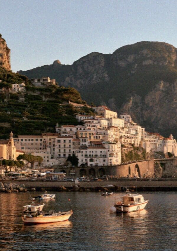 The town of Amalfi seen from the sea at golden hour, houses stacked on the cliff above the harbour