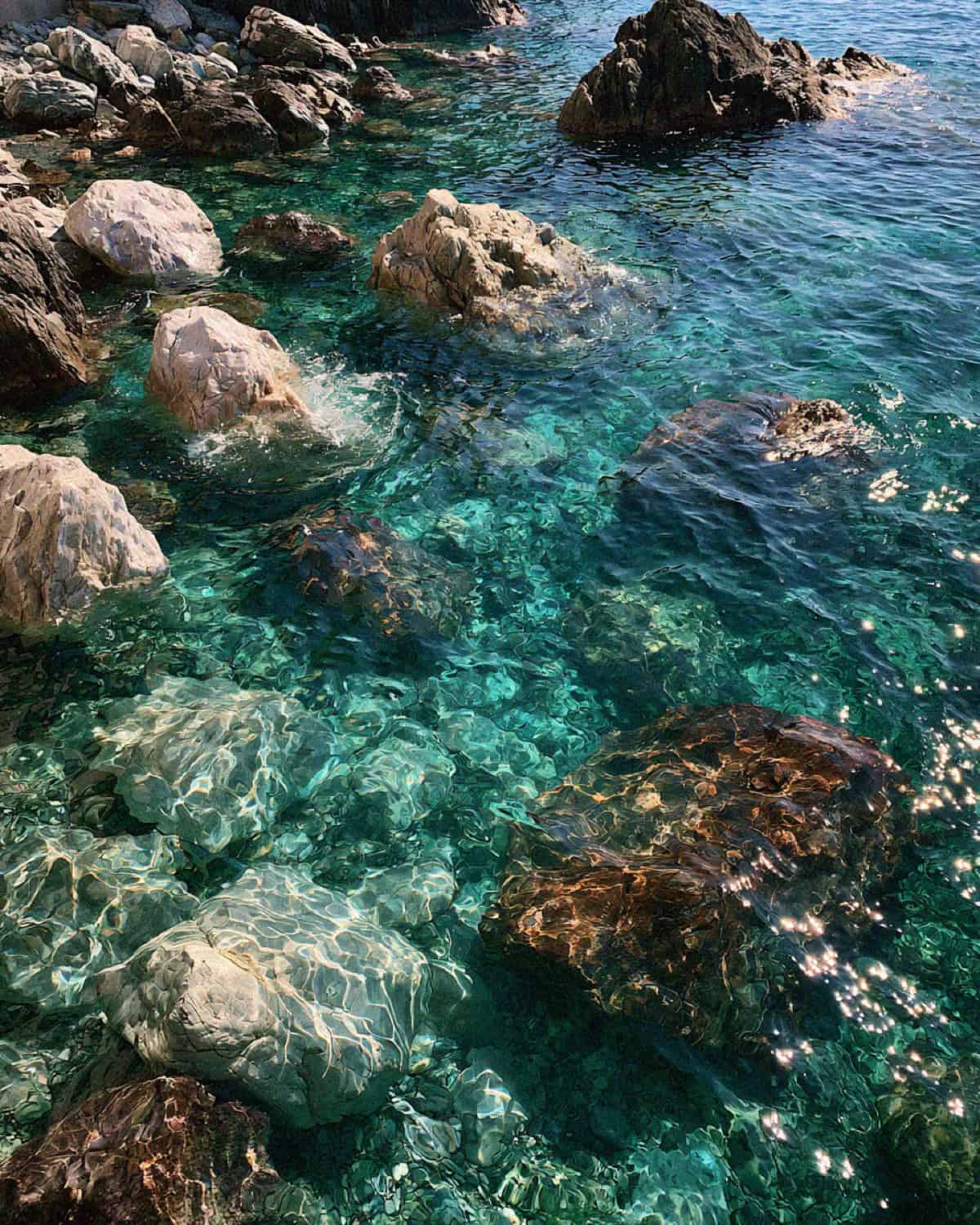 Crystal clear turquoise water over rocks in a cove on the Cinque Terre coast