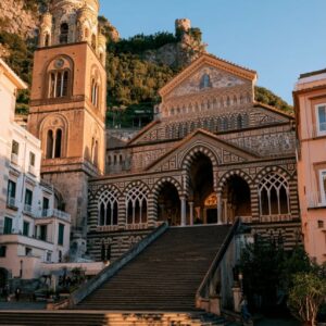 The black and white striped Arab-Norman facade of the Duomo di Amalfi Cathedral of Sant'Andrea rising above the grand stone steps of Piazza del Duomo at golden hour