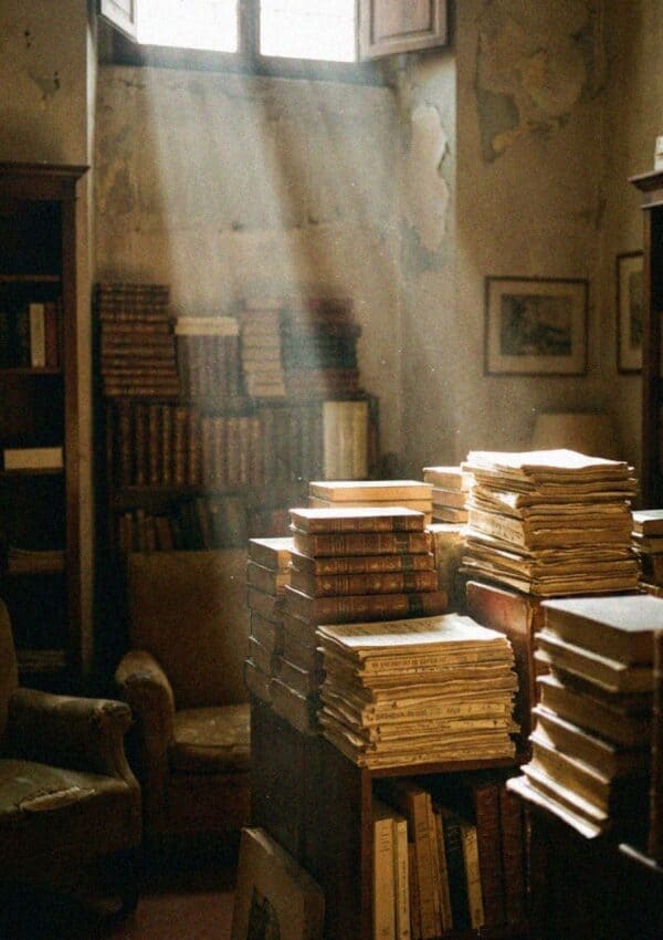 A dim Florentine antiquarian bookshop stacked with old books in shafts of light