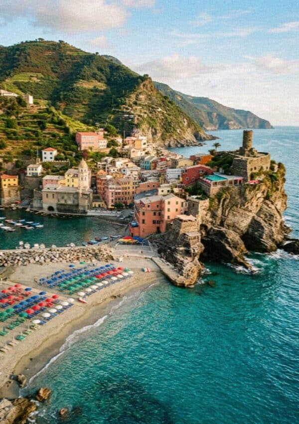 The beach and umbrellas of Monterosso al Mare in Cinque Terre with the headland tower beyond