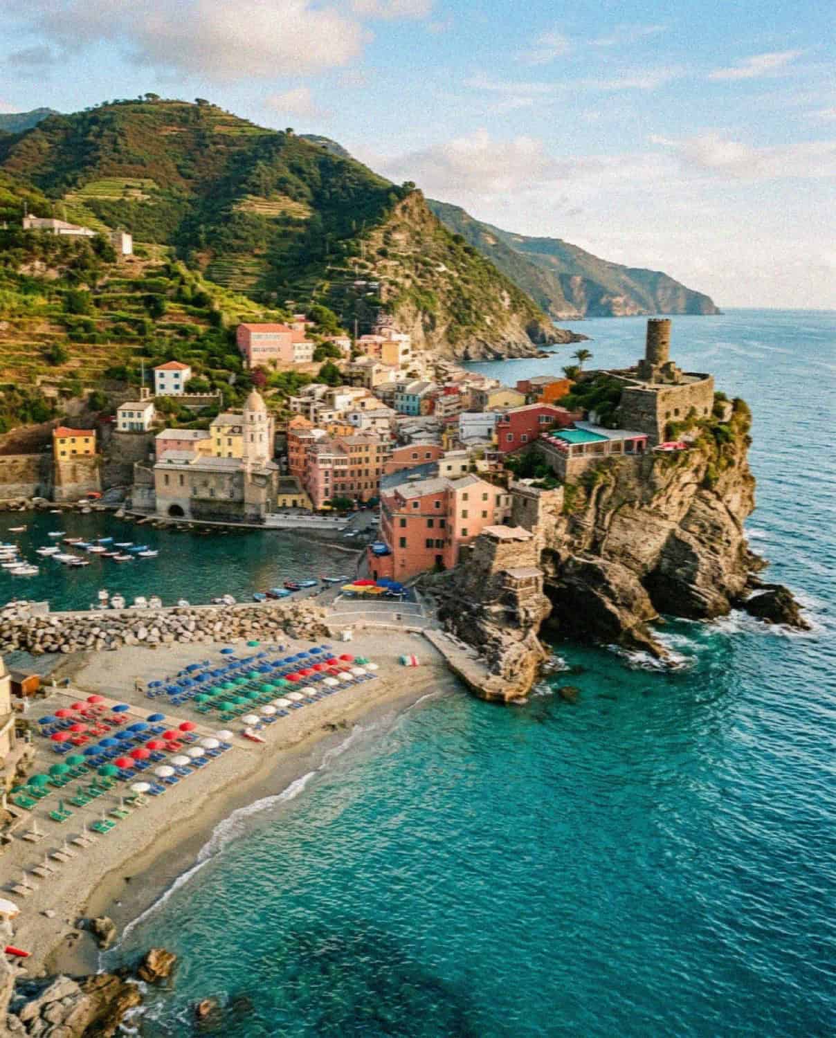 The beach and umbrellas of Monterosso al Mare in Cinque Terre with the headland tower beyond
