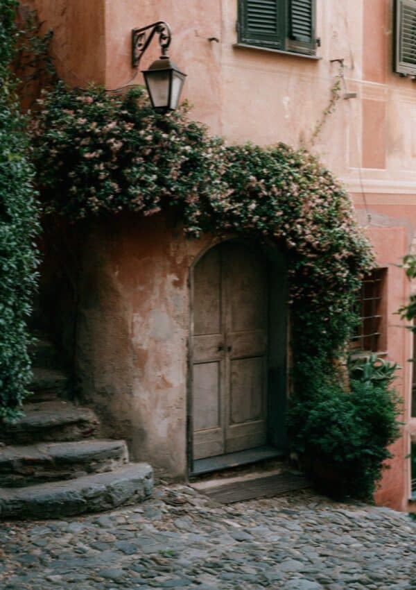 A pastel Portofino building with an arched wooden door and ivy