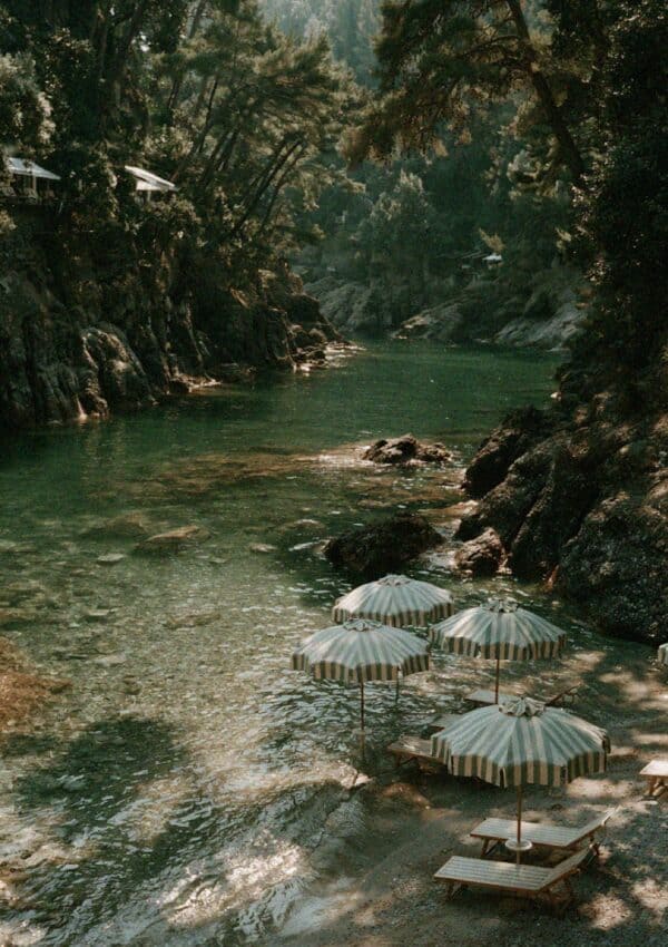 Rows of green and white striped umbrellas on the pebble shore of an emerald cove near Portofino