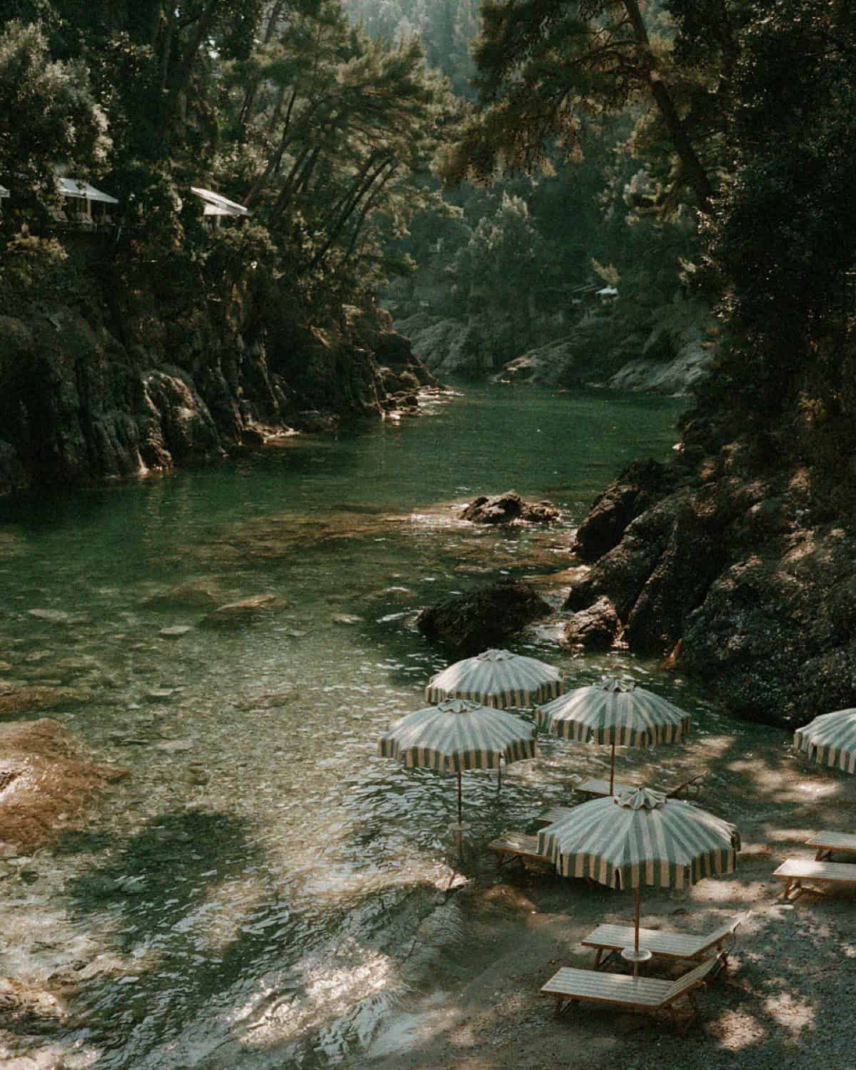 Rows of green and white striped umbrellas on the pebble shore of an emerald cove near Portofino
