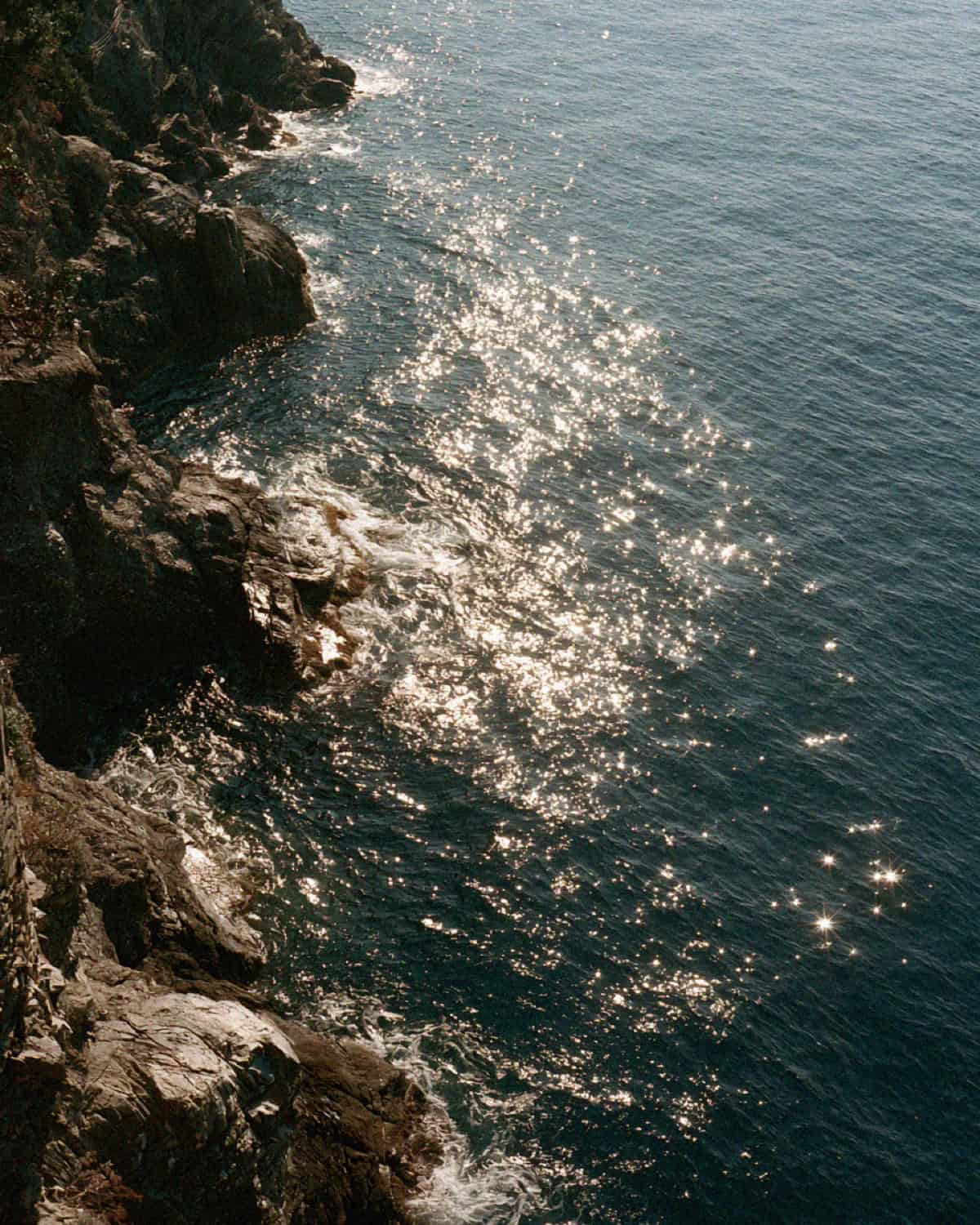 Sunlight sparkling on the deep blue sea off a rocky headland near Portofino