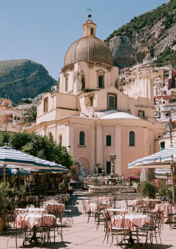The golden domed church of Positano rising above the piazza with cafe umbrellas and pink tablecloths on the Amalfi Coast