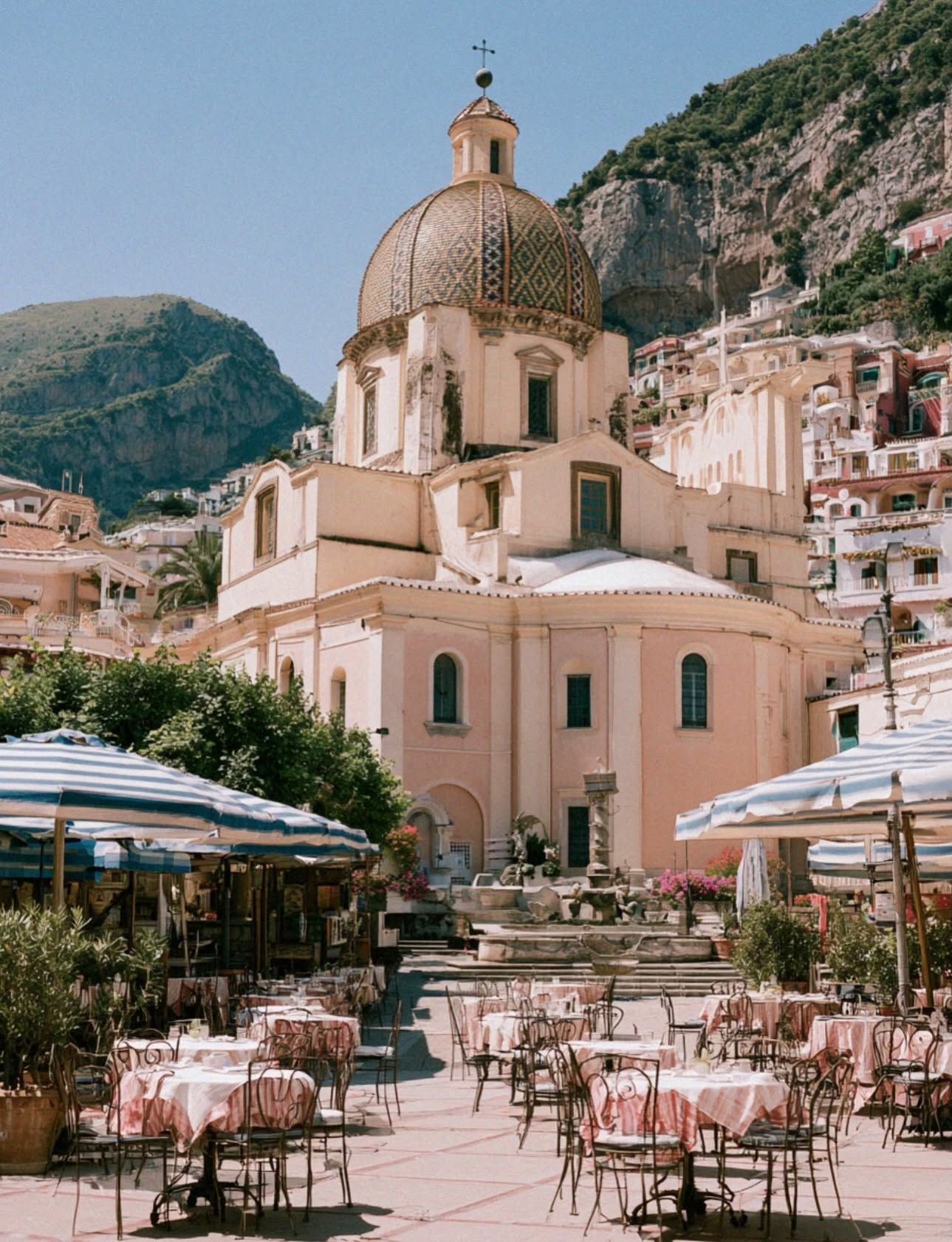 The golden domed church of Positano rising above the piazza with cafe umbrellas and pink tablecloths on the Amalfi Coast