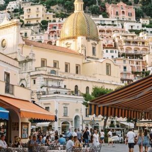 Positano's golden domed church rising above the piazza with striped market umbrellas at golden hour