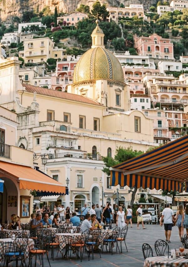 Positano's golden domed church rising above the piazza with striped market umbrellas at golden hour