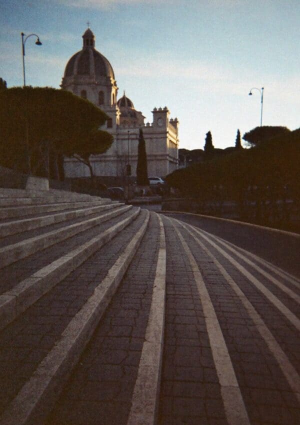 A domed church above a sweeping stepped street in Rome at dusk