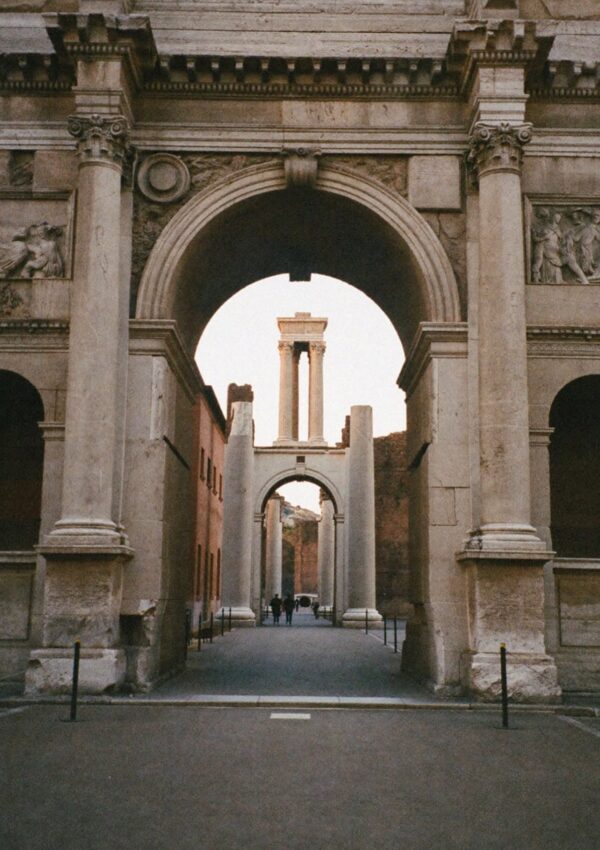 An ancient Roman arch framing columns and a street in Rome