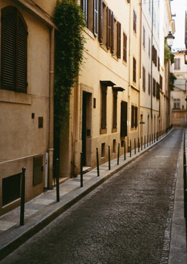A quiet ochre lane with bollards and green ivy in Rome
