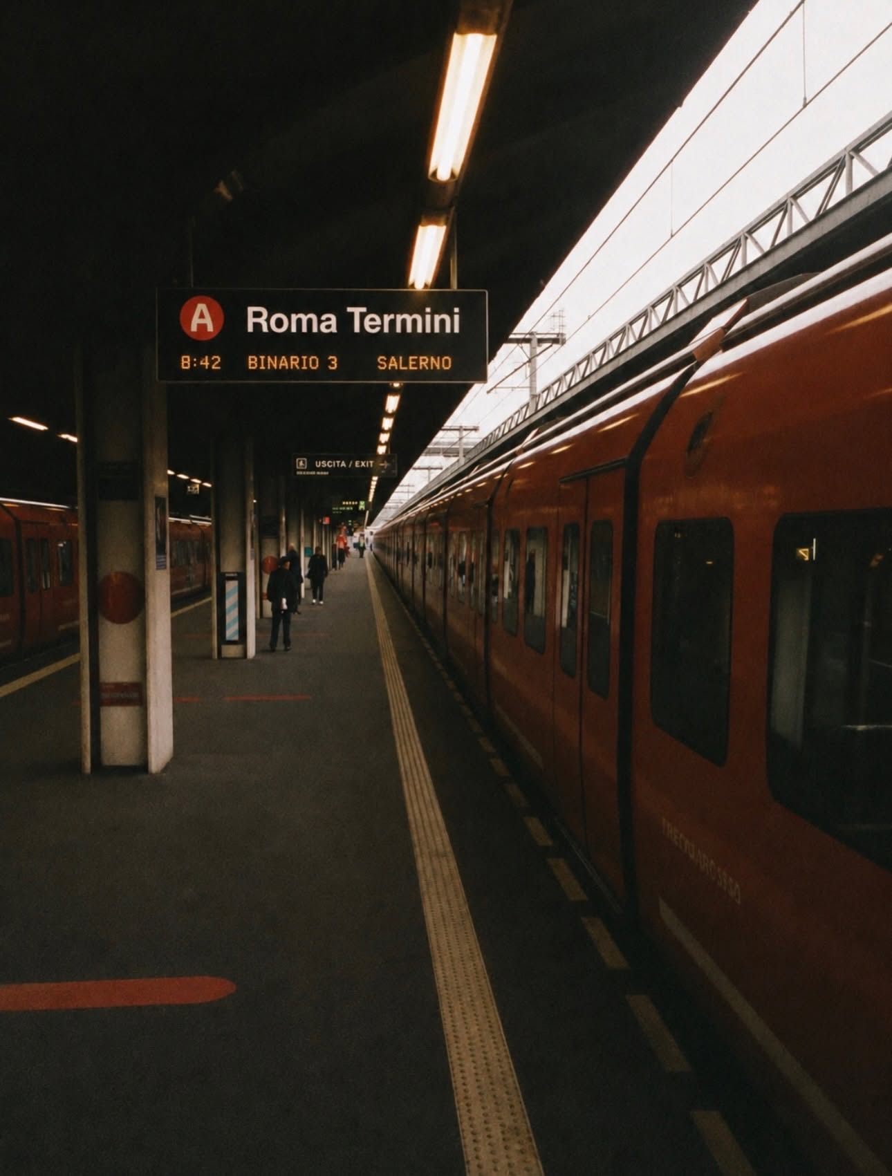 A red train at the platform of Roma Termini station beneath the departures sign