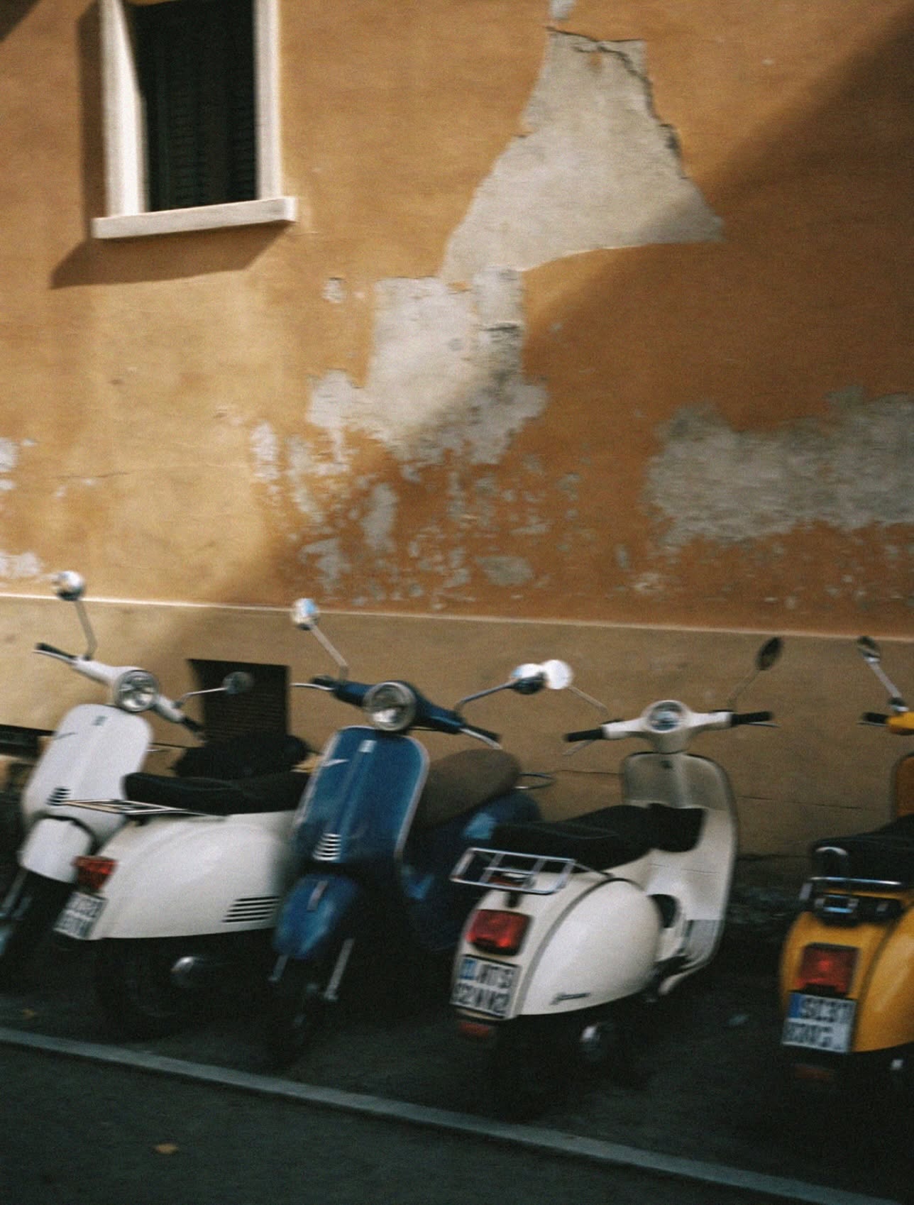 Vintage Vespa scooters parked against a peeling ochre wall in Rome