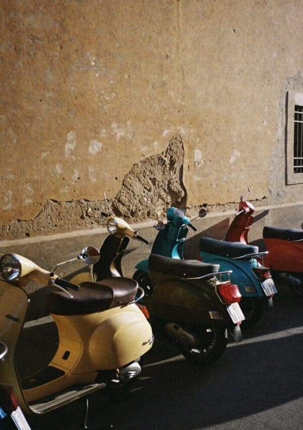 A row of vintage Vespa scooters parked against a cracked ochre wall in Rome
