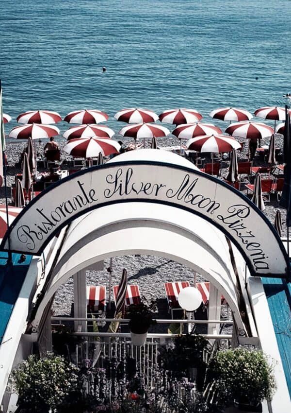 The arched entrance of Ristorante Silver Moon Pizzeria in Amalfi framing rows of red and white striped umbrellas on the pebble beach with the Tyrrhenian Sea beyond