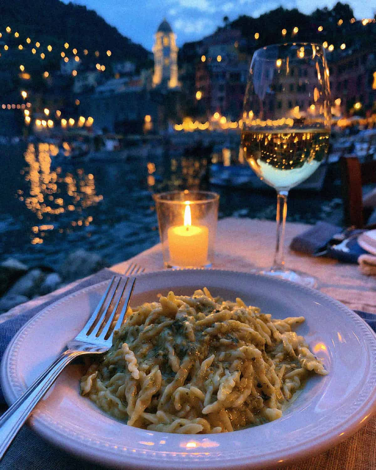 A plate of trofie al pesto and white wine at a harbourside table in Vernazza at dusk