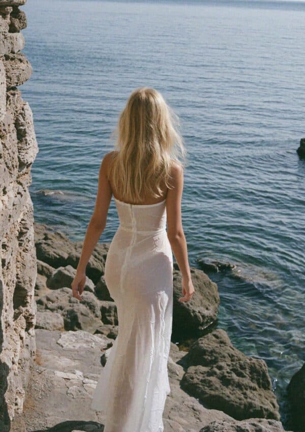 Victoria Van Der Berg in a white gown on the rocks by the sea below Amalfi