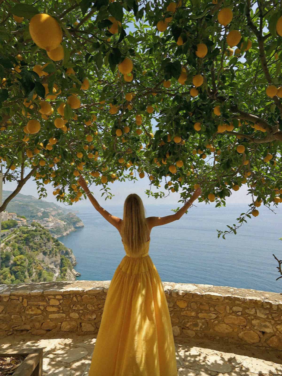 Victoria Van Der Berg in a yellow dress under a lemon tree above the Amalfi Coast