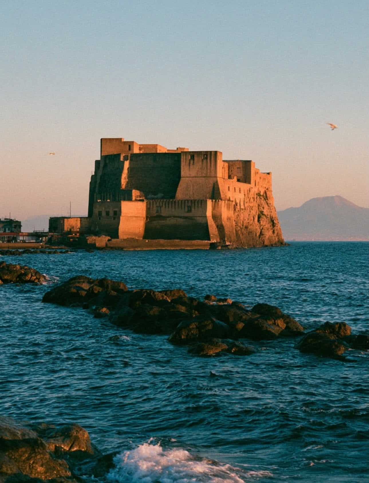 Castel dell'Ovo glowing amber at sunset with Mount Vesuvius across the Bay of Naples