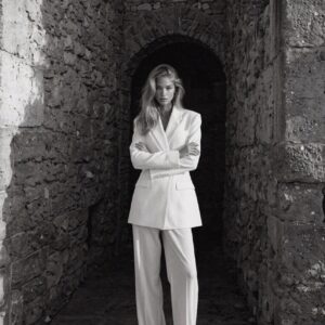 Victoria Vanderberg in a white blazer suit standing beneath a stone archway in Ravello