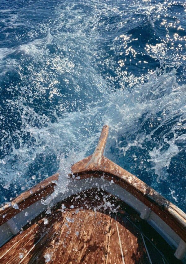 The bow of a wooden boat cutting through sparkling blue sea off the Cinque Terre coast