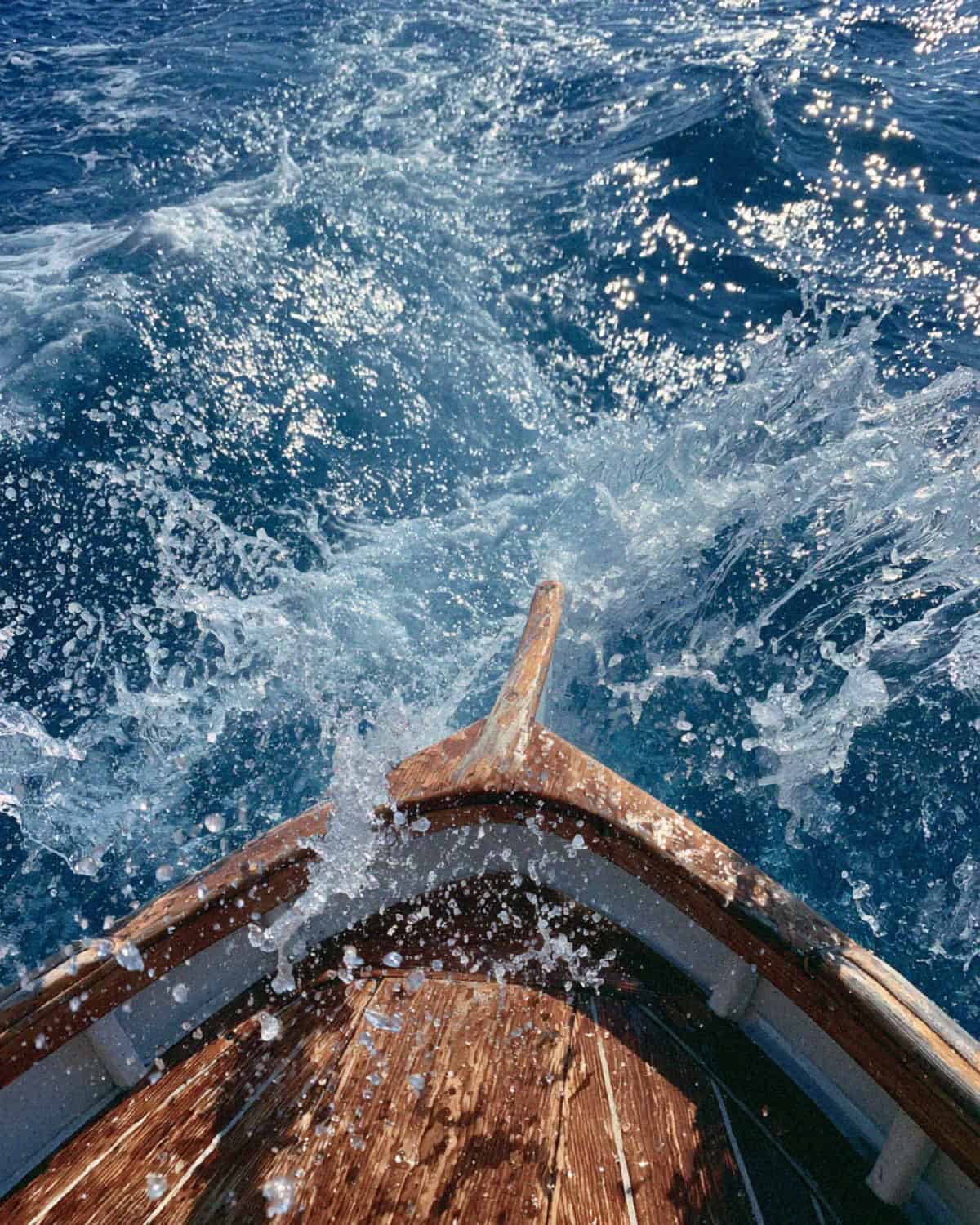The bow of a wooden boat cutting through sparkling blue sea off the Cinque Terre coast