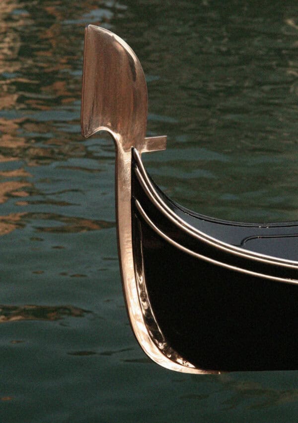 Black gondola with its steel ferro prow on a green Venice canal