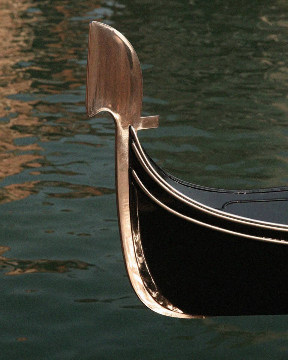 Black gondola with its steel ferro prow on a green Venice canal