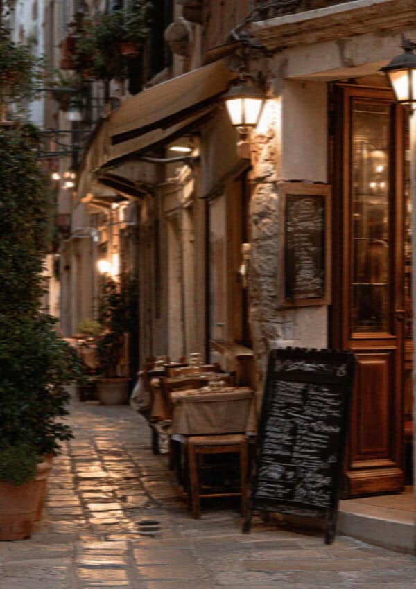 Narrow Venice street with a cafe, a lantern and a chalkboard menu in warm light