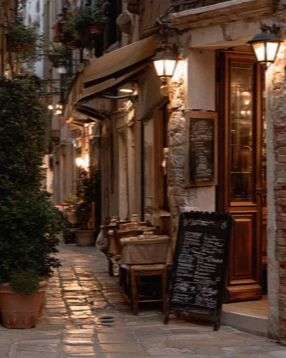 Narrow Venice street with a cafe, a lantern and a chalkboard menu in warm light