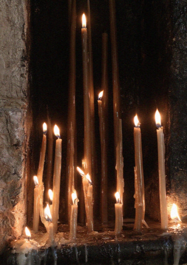 A bank of thin lit tapers burning in a blackened stone niche in Assisi