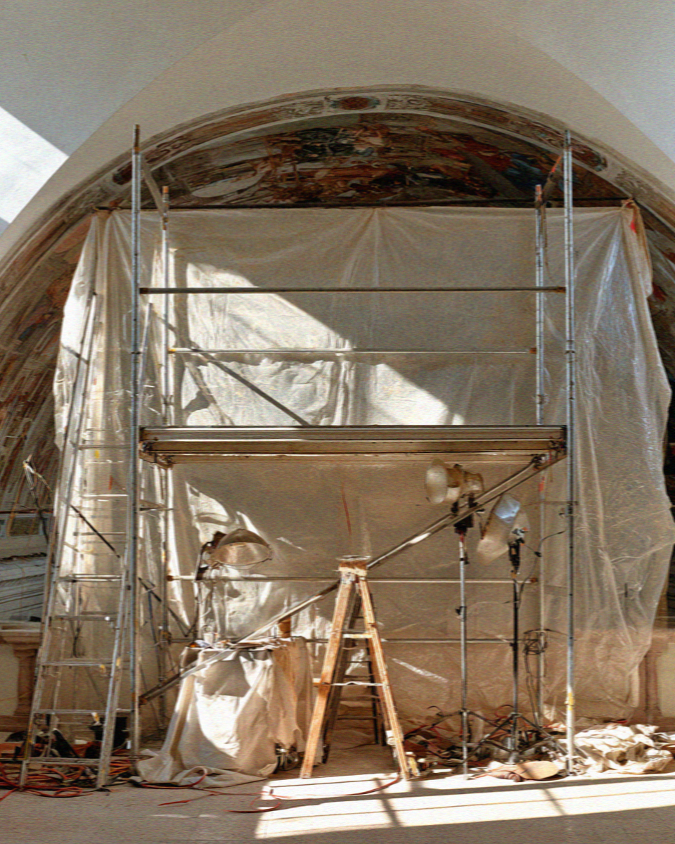Restoration scaffolding and dust sheets standing against a frescoed vault inside the basilica at Assisi