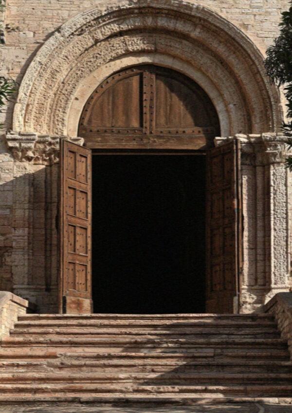 A deep carved medieval stone portal in Assisi with worn steps and heavy timber doors standing open