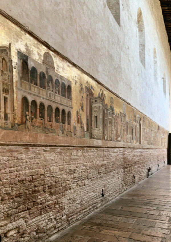 A long wall of medieval frescoes running at eye level in raking light in Assisi