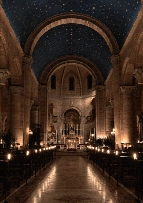 The dark Lower Basilica in Assisi with its deep blue vault of gold stars and rows of lit candles down the nave