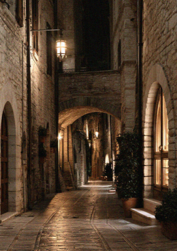 A medieval Assisi lane at night with warm lantern light on pale stone